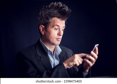 Handsome Man With Mohawk Wearing Suit Using Mobile Phone In Front Of Black Background.