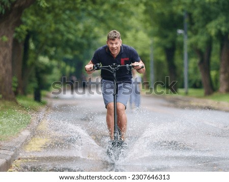 Handsome man in the Moscow public park in summer day after the rain. Water splashes from the puddle around him. He riding motor scooter. Leisure time and lifestyle concept. Frontal view