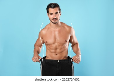 Handsome man with muscular body in oversized jeans on light blue background. Weight loss - Shutterstock ID 2162714651
