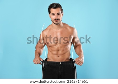Handsome man with muscular body in oversized jeans on light blue background. Weight loss