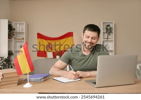 Handsome man with notebook and flag of Spain learning language online at table