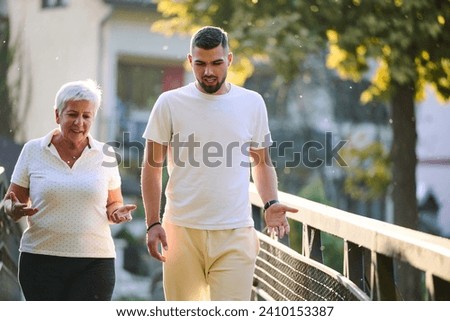 A handsome man and an older woman share a serene walk in nature, crossing a beautiful bridge against the backdrop of a stunning sunset, embodying the concept of a healthy and vibrant intergenerational