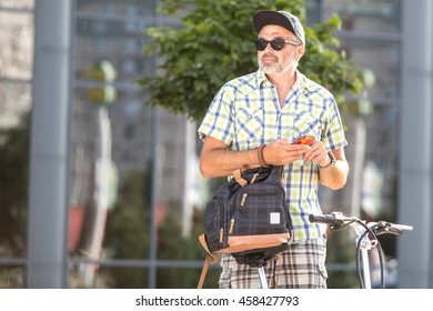 Handsome Man On Bike In The City On A Sunny Day Holding A Smart Phone And Waiting For A Girlfriend