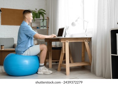 Handsome man on fitball working with laptop at home