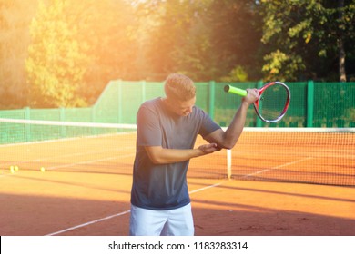 Handsome Man On Tennis Court. Young Tennis Player. Pain In The Elbow With Sunlight In Background