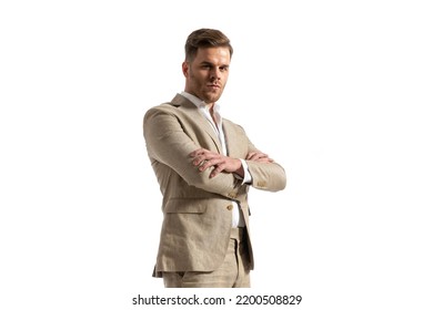 Handsome Man With Open Collar Shirt Wearing Beige Suit, Folding Arms And Posing Isolated On White Background In Studio