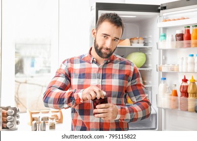 Handsome Man Opening Jar Near Refrigerator In Kitchen