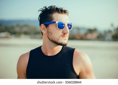 Handsome man outdoors portrait.Stylish man posing on the beachfront and ready for surfing.Happy and active.Summer sunglasses,Young sportsman,young surf man,wetsuit and surf shorts,Cool man with beard - Powered by Shutterstock