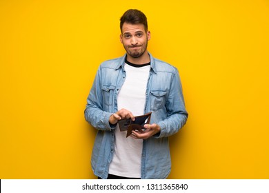 Handsome man over yellow wall holding a wallet