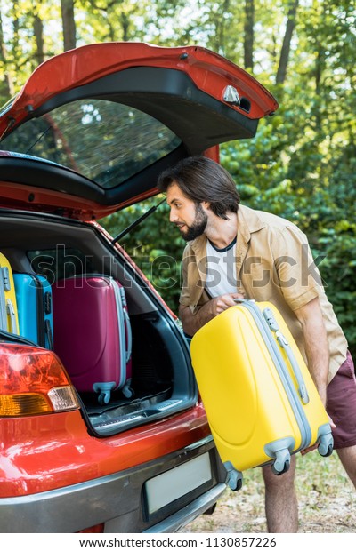 handsome man\
packing car trunk with travel\
bags