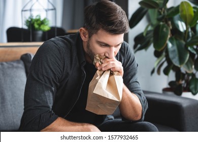 handsome man with panic attack breathing in paper bag in apartment 