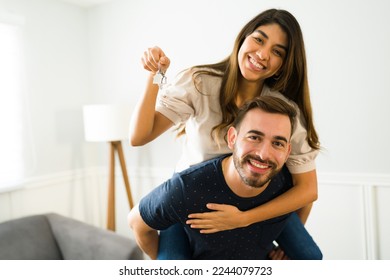 Un hombre guapo pigenta respaldando a su novia mostrando sus nuevas llaves de casa después de comprar una casa
