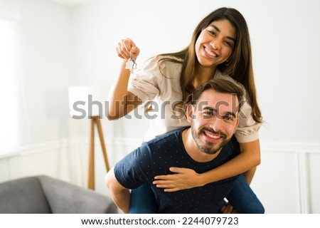 Handsome man piggybacking his girlfriend showing their new home keys after buying a house