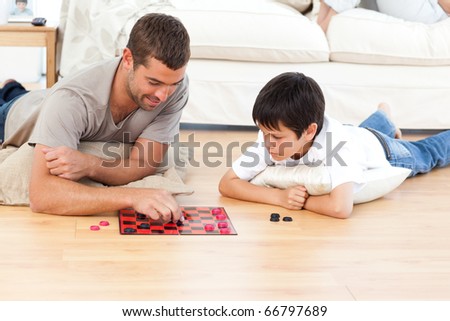 Handsome man playing checkers with his son lying on the floor at home