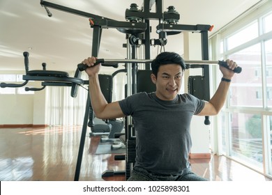 Handsome man playing with fitness machine in gym. Bodybuilder man doing heavy weight exercise with machine with cable in fitness club.