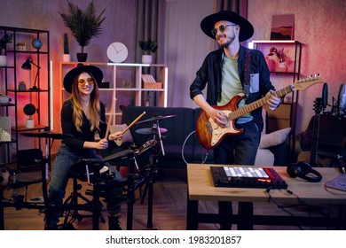 Handsome man playing guitar while beautiful woman playing electronic drums at studio. Group of two musicians in stylish outfit rehearsing together indoors. - Powered by Shutterstock