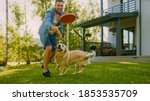 Handsome Man Plays Catch flying disc with Happy Golden Retriever Dog on the Backyard Lawn. Man Has Fun with Loyal Pedigree Dog Outdoors in Summer House Backyard.