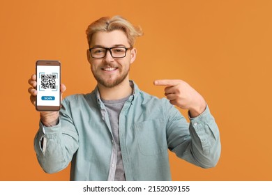 Handsome man pointing at smartphone with QR code on screen against orange background