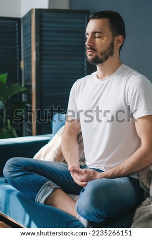 Handsome man practicing meditation in the cross-legged posture, on the sofa in his living room. Breathing exercise.