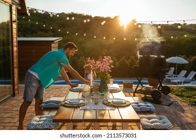 Handsome man putting plate on the table and serving the table before the family dinner in the backyard - Shutterstock ID 2113573031