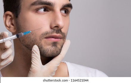 Handsome Man Receiving Filler Injection In His Face On Grey Background