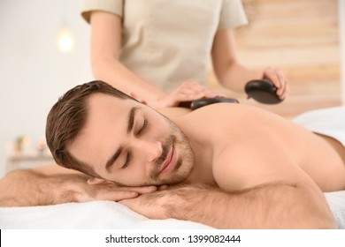 Handsome Man Receiving Hot Stone Massage In Spa Salon