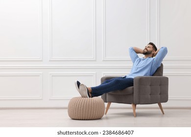 Handsome man relaxing in armchair near white wall indoors, space for text - Powered by Shutterstock