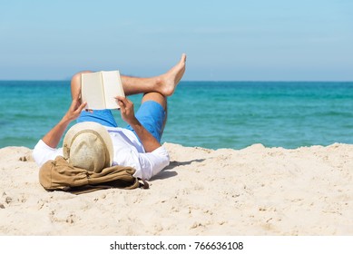 Ein gut aussehender Mann, der sich in einem Buch entspannt, das am Strand liest.