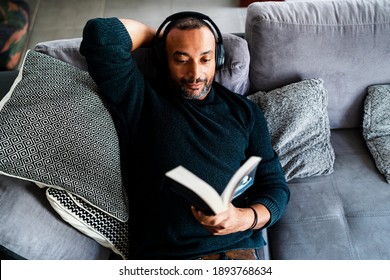 Handsome man relaxing on the sofa at home with a book and headphones - Powered by Shutterstock