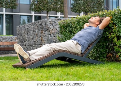 Handsome man relaxing on wooden chaise lounge in city park. Life-work balance and lifestyle concept of business man lying, take it easy near office or hotel room resting with thoughtful mind.