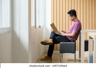Handsome man relaxing using computer laptop while sitting on chair  beside window in office