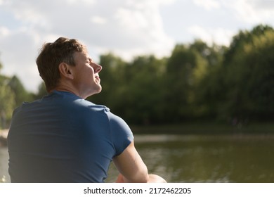 Handsome Man Resting In The Moscow Public Park In Front Of Th. He Is Sunbathing In Sunny Summer Day. He Closed Eyes. Concept Of The Happiness And Full Relaxation. Back Rear View