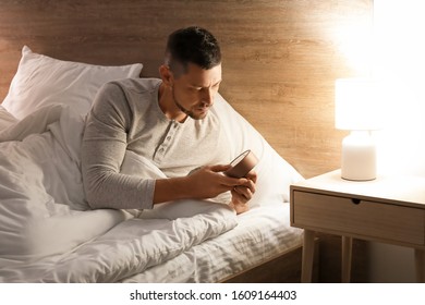 Handsome man setting an alarm while lying in bed at night - Shutterstock ID 1609164403