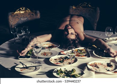 Handsome Man Or Sexy Muscular Macho Athlete Bodybuilder With Muscle Torso Undressed To Waist Lying On Table With Leftovers Or Residues Food On Dirty Plates After Banquet In Restaurant