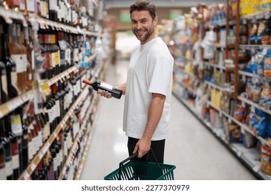 Handsome man with shopping basket with grocery. Man choosing alcohol bottles at liquor store. - Powered by Shutterstock