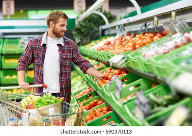 Handsome man with shopping trolley touching tomato in order to define its quality in fruit and vegetable department of supermarket - Powered by Shutterstock