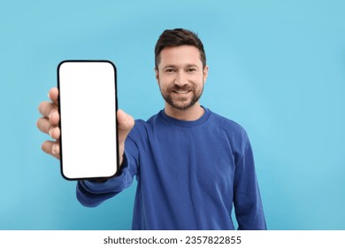 Handsome man showing smartphone in hand on light blue background - Powered by Shutterstock