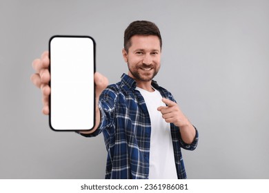 Handsome man showing smartphone in hand and pointing at it on light grey background - Powered by Shutterstock