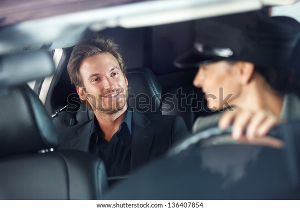 Handsome man sitting in luxury car, female\
chauffeur driving.