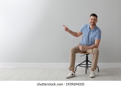 Handsome Man Sitting In Office Chair Near Grey Wall Indoors, Space For Text