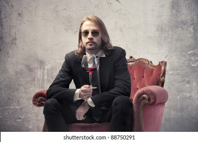 Handsome man sitting on an armchair and holding a glass of wine - Powered by Shutterstock