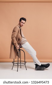 Handsome Man Sitting On The Chair, Portrait Of Young Man In A Beige Coat, Beige Background