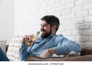 Handsome Man Sitting Relaxed On A Sofa While Is Drinking A Beer.