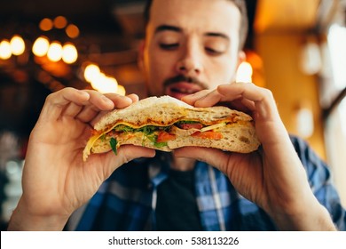 Handsome man sitting in a restaurant and looking at hamburger. He is going to taste that big delicious dish. Young guy having his lunch