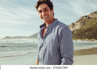 Handsome man smiling on the beach on a summer day. Man in checkered shirt standing on the beach and looking at the beach. - Powered by Shutterstock
