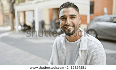 Handsome man smiling on a city street while wearing a white cardigan in a candid urban setting.