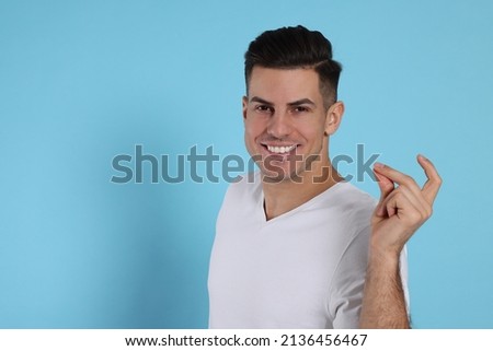 Handsome man snapping fingers on light blue background. Space for text