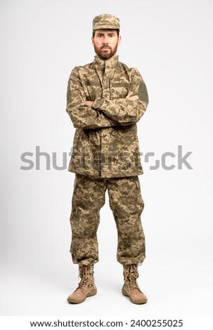 Handsome man, soldier wearing camouflage military uniform, boots holding arms crossed looking at camera isolated on white background