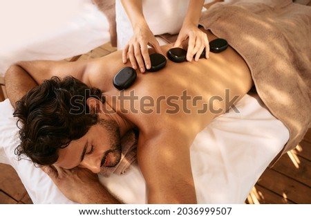 Handsome man at spa resort receives hot stone massage. Hot stone massage therapy using smooth, flat, heated stones