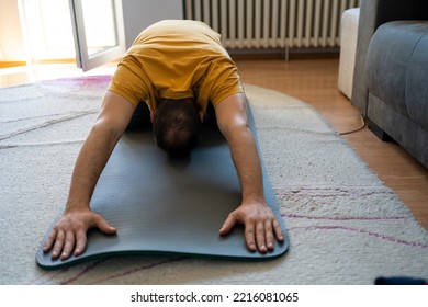 Handsome Man In Sports Clothes Is Stretching On Yoga Mat While Working Out At Home. Sporty Man Stretching Back Before Home Workout. Doing Back Stretching. Fitness Strong Male Athlete On Floor Mat 